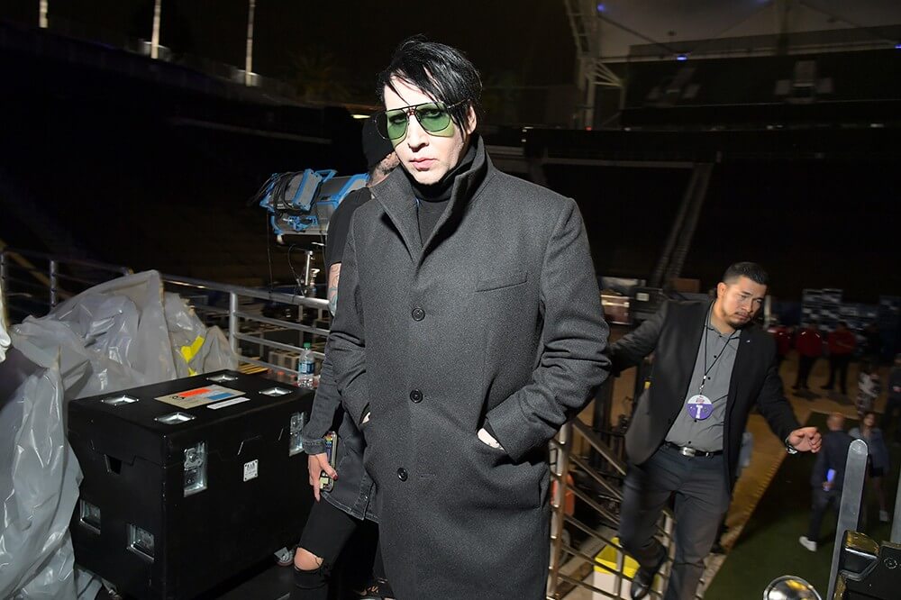 Marilyn Manson dengan coat hitam dan kacamata berlensa hijau